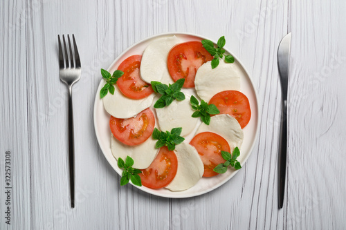 Salad caprese on white plate on light wooden table. Close up. 