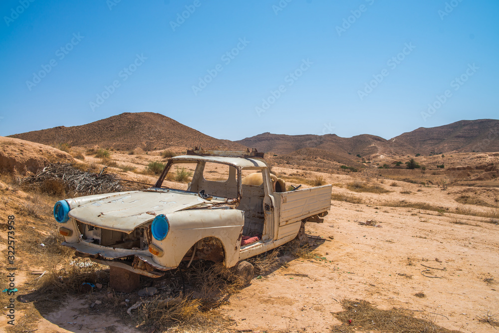 A car abandoned in the desert.
Wide plans for a great sunny space full of sand and a rusty, damaged car.