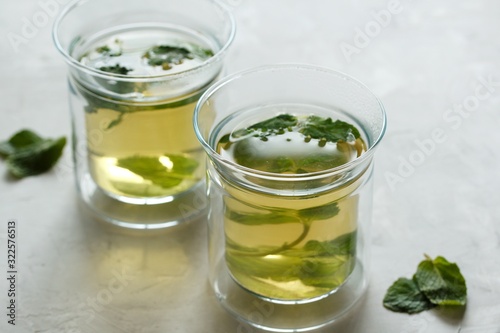 Two glass cups with green tea with mint on a light gray table