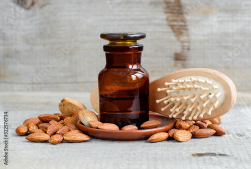 Pharmacy bottle with almond oil, almonds and wooden hair brush. Natural hair care concept. Old wooden background. Almonds close up. Copy space