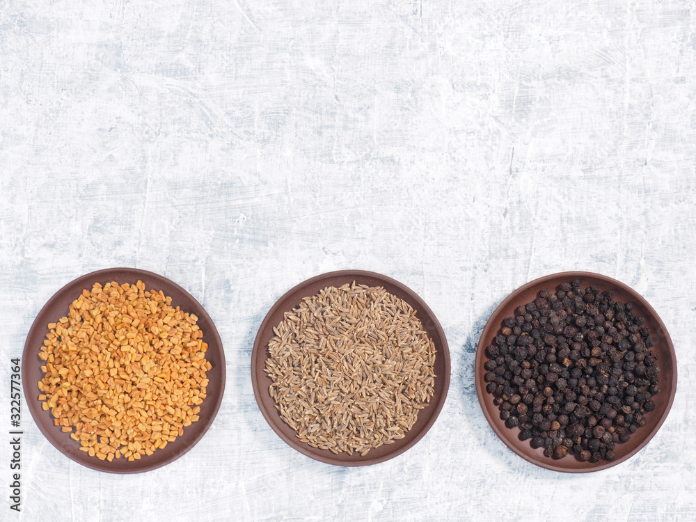 Spice fenugreek, cumin (jeera), black pepper in clay plate on white concrete background Spice fenugreek, cumin (jeera), black pepper in clay plate on white concrete background