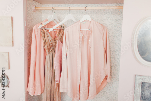 wooden pink wardrobe for women’s clothes, open doors, decor, mirror, bag, hangers, silk dresses in a bright room, concept, flowers delicate pastel colors