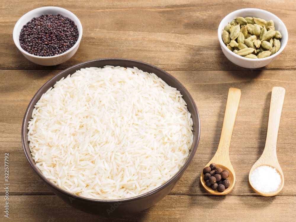 Long grain Basmati rice in brown ceramic bowl, allspice, green cardamom, mustard seed, salt on brown wooden background Long grain Basmati rice in brown ceramic bowl, allspice, green cardamom, mustard seed, salt on brown wooden background