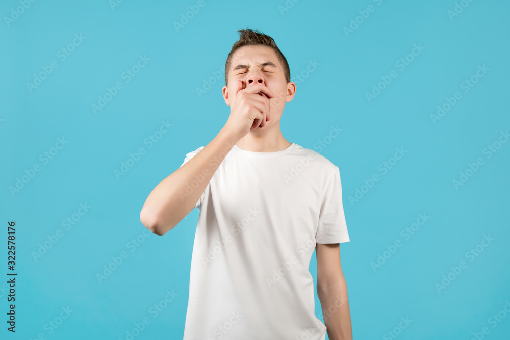 teenager yawns, closing his mouth with his fist