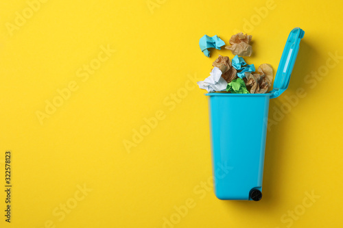 Recycle bin with trash on yellow background, space for text photo