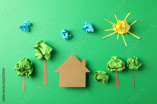 Paper house, clouds, sun and trees on green background, top view photo