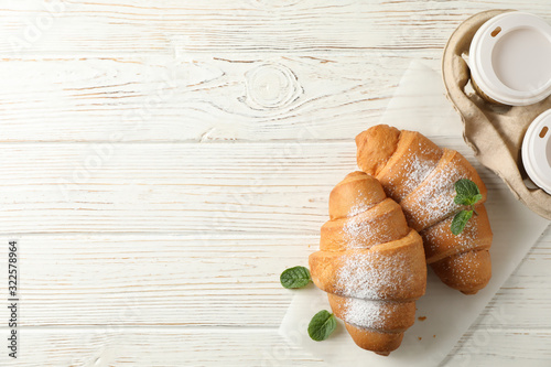 Tasty croissants and cups with coffee on wooden background, top view