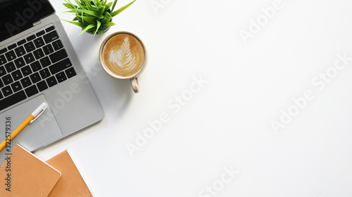 Top view of white working table with office equipment putting on it. Flat lay Computer laptop, Coffee cup, Potted plant, Notebook and pencil. Modern and comfortable working desk concept.