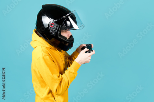 Fototapeta Naklejka Na Ścianę i Meble -  side view of a teenager in a motorcycle helmet with a joystick from a game console