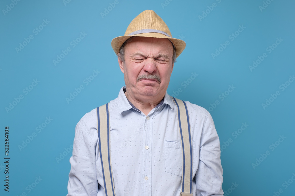 Senior man in summer hat with disgusted expression repulsing something. Disgust concept. Human emotions, facial expression concept. Studio shot blue wall. Senior man in summer hat with disgusted expression repulsing something. Disgust concept. Human emotions, facial expression concept. Studio shot blue wall.
