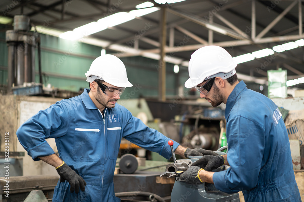 Industrial engineers in safety uniforms wearing white safety helmets are inspecting work by tools.  and on the job training he works in industrial machinery.