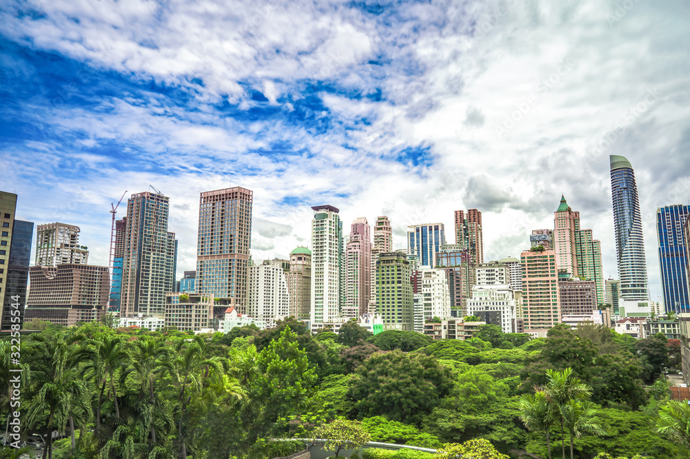 Green area in front of the middle of Bangkok metropolis with high building all around in the open sky.