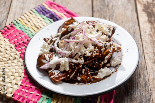 Mexican chilaquiles with mole sauce and fresh cheese on wooden background