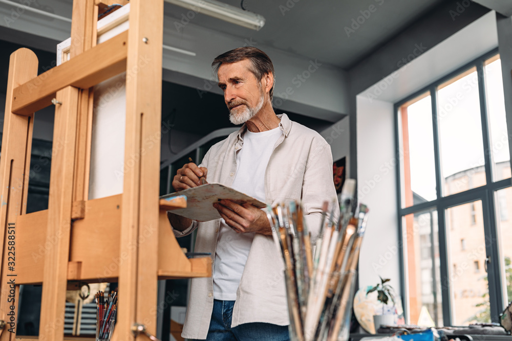 Male painter standing in his studio at an easel and looking on canvas Male painter standing in his studio at an easel and looking on canvas