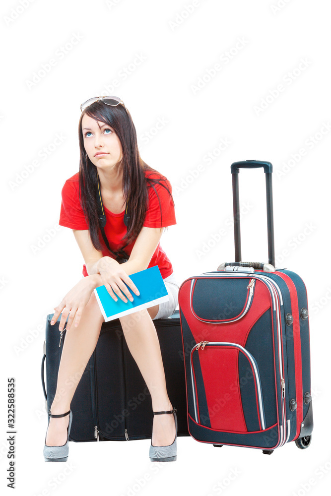Difficult waiting. A beautiful young woman in a red blouse and white skirt, sitting on suitcases, tired of waiting for her flight, isolated on a white background. Blue ticket to fly/ Difficult waiting. A beautiful young woman in a red blouse and white skirt, sitting on suitcases, tired of waiting for her flight, isolated on a white background. Blue ticket to fly/