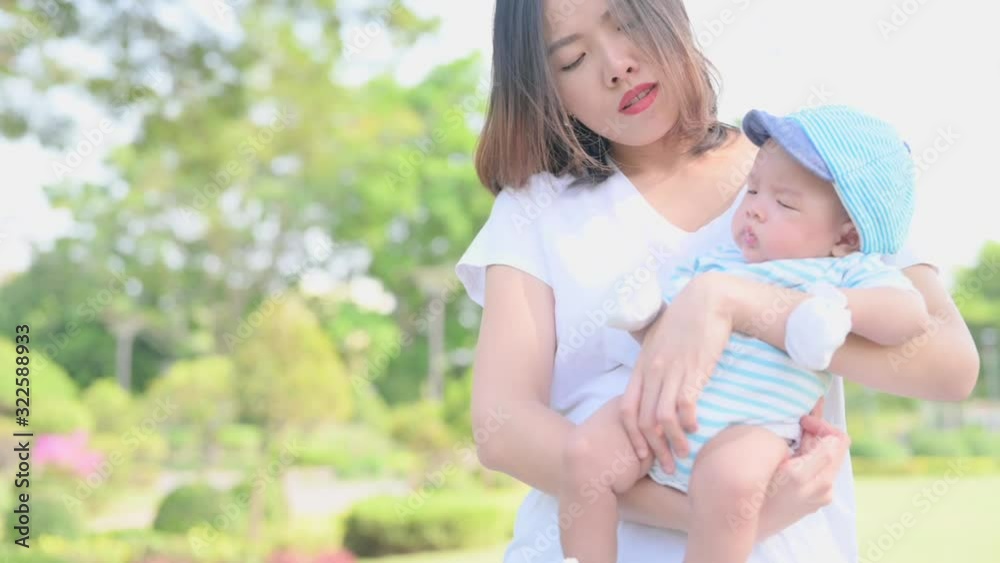 Slow motion of a asian mother smiling with her 3 months old baby boy on green grass outdoor in park. Slow motion of a asian mother smiling with her 3 months old baby boy on green grass outdoor in park.