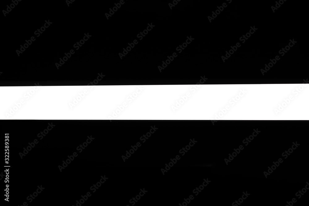 Modern white neon wall or ceiling lamp in the form of a long stripe in a dark room. Horizontal abstract geometric shape and line on a black background