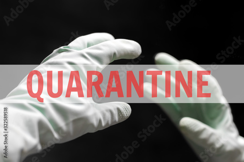 A hand in a mint green rubber glove reaches for its reflection in the mirror in the dark black room. In the center of the photo is a white transparent stripe with a red inscription: quarantine