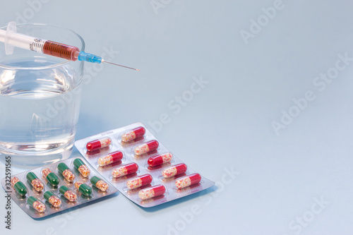 Tablets in blister pack, syringe with vaccine and glass of water on blue background. photo