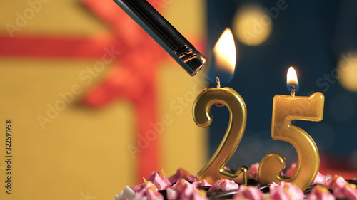 Birthday cake number 25 golden candles burning by lighter, background gift yellow box tied up with red ribbon. Close-up