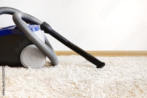 Canister modern vacuum cleaner blue for cleaning the house on the background of the wall and soft carpet. Equipment, room cleaning. Copy space for text.