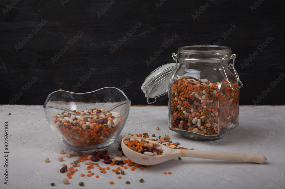 Legumes White and red beans, lentils, peas in a glass jar and in a glass cup, sprinkled beans and a wooden spoon on a white table on a black background. Healthy eating Legumes White and red beans, lentils, peas in a glass jar and in a glass cup, sprinkled beans and a wooden spoon on a white table on a black background. Healthy eating