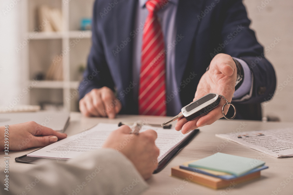 selective focus of agent holding car key near client signing contract