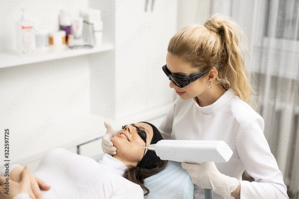 Cosmetologist in white gloves applying make up for woman in beauty salon. Laser peeling of a face. Skin care. Fashion, beauty, makeup, cosmetics, health, spa, wellness. Cosmetologist in white gloves applying make up for woman in beauty salon. Laser peeling of a face. Skin care. Fashion, beauty, makeup, cosmetics, health, spa, wellness.