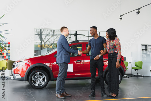 salesman showing new car to african couple in showroom © Serhii