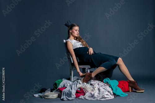 woman in the crown is sitting on a pile of clothes as the queen of consumerism