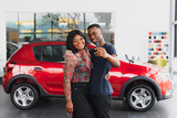 happy african couple choosing luxury car at vehicle dealership looking at the interior