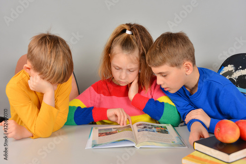 Three children read a book and do their homework assigned at school.