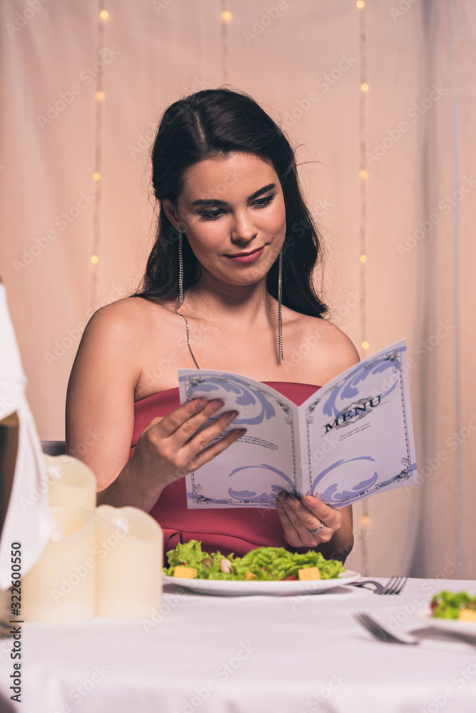 attractive, elegant girl reading menu while sitting in restaurant