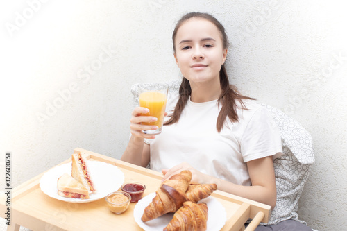 Happy morning. A young woman eats a delicious Breakfast in bed - fresh croissants, coffee, orange juice and muesli with fruit.