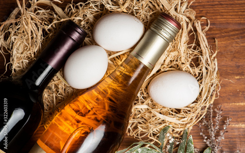 Canvas Print Wine bottles and chicken eggs in hay  on the wooden background.