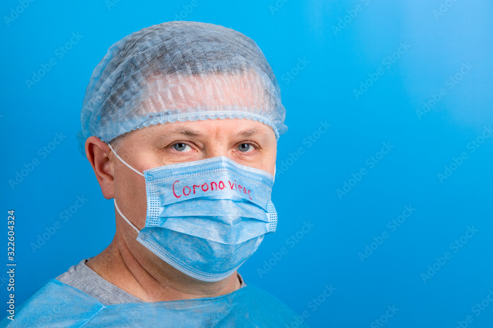 Portrait of man wearing medical uniform and mask with coronavirus word at blue background. Protect your health. Coronavirus concept with copy space Portrait of man wearing medical uniform and mask with coronavirus word at blue background. Protect your health. Coronavirus concept with copy space