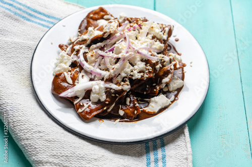 Mexican chilaquiles with mole sauce and fresh cheese on turquoise  background