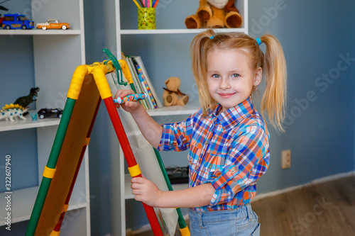 smiling child girl blonde draws on a white Board with a felt-tip pen at home. Concept of preschool education and development