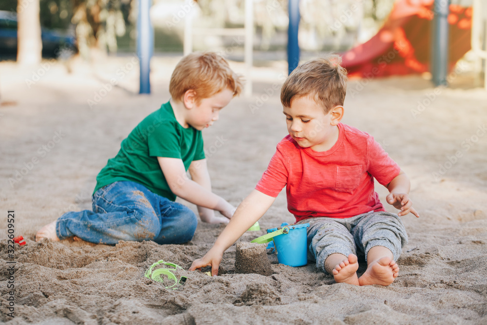 Two Caucasian children sitting in sandbox playing with beach toys. Little boys friends having fun together on playground. Summer outdoors activity for kids. Leisure time lifestyle childhood. Two Caucasian children sitting in sandbox playing with beach toys. Little boys friends having fun together on playground. Summer outdoors activity for kids. Leisure time lifestyle childhood.