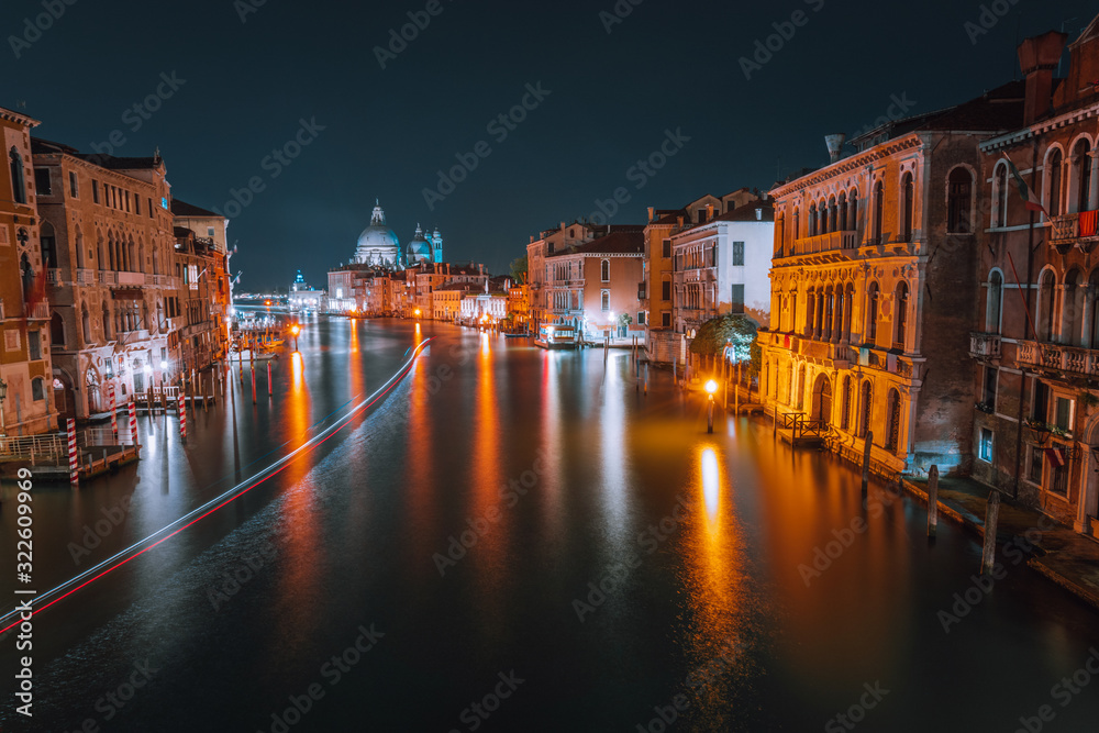 Venice, Italy night scenery of Grand Canal. Vivid light trails of ferries and boats reflected on water surface. Majestic Basilica di Santa Maria della Salute in background