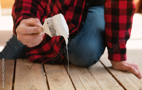 man paint a wood plank with white liquid color