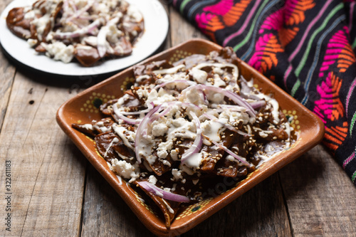 Mexican chilaquiles with mole sauce and fresh cheese on wooden background photo