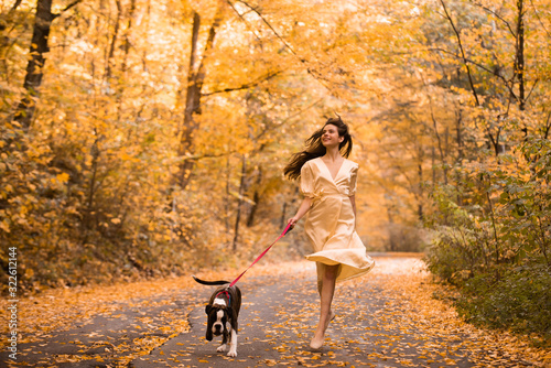 Young woman with the dog in the park. Wind in the hair. With dog on a walk in an autumn nature. Young beautiful female having fun in autumn park. Girl enjoy walk with dog. Favorite pet. © Volodymyr