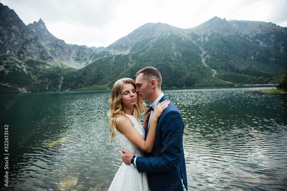 Sensual wedding couple standing on the stony shore of the Sea Eye lake in Poland.