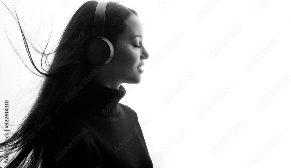 Fototapeta premium Beautiful woman in headphones listening music with closed eyes. Black and white. Free space for text.