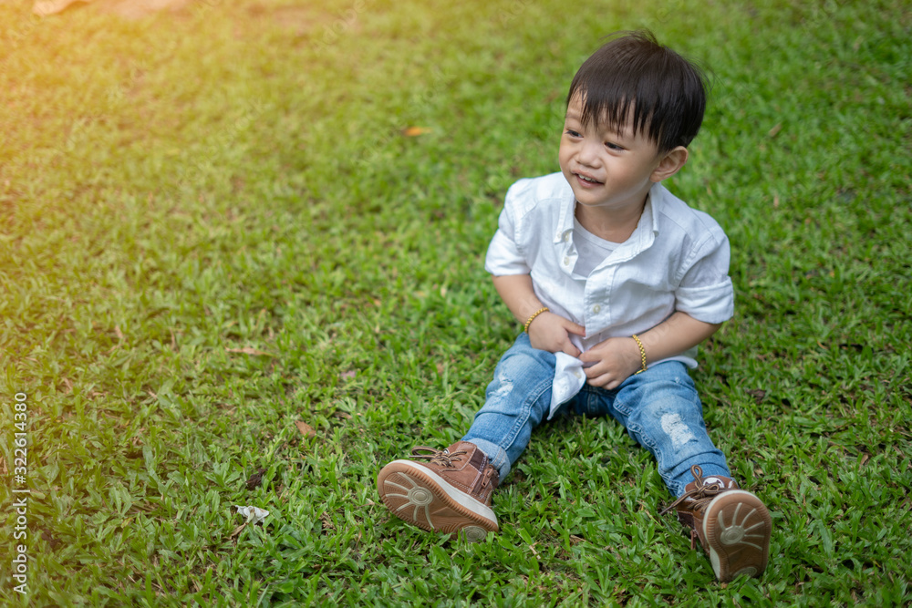 Asian boy Wearing a white shirt Sitting on the lawn Smiling happily Asian boy Wearing a white shirt Sitting on the lawn Smiling happily