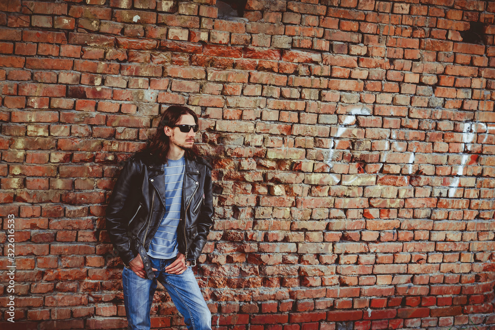 a man in a leather jacket against a brick wall a man in a leather jacket against a brick wall