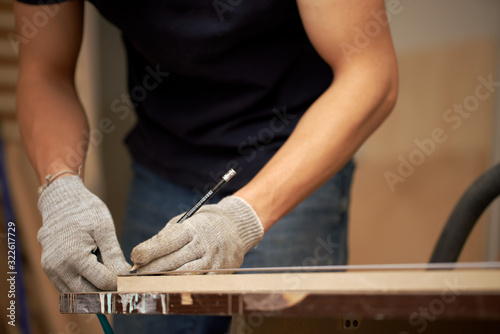 Male carpenter holds narrow board in his workshop