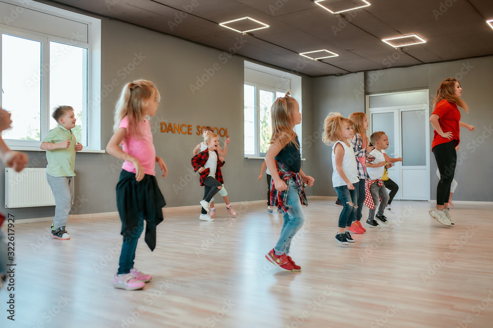 Repeat after me. Group of active children dancing in front of the large mirror while having choreography class in the dance studio. Female dance teacher and kids