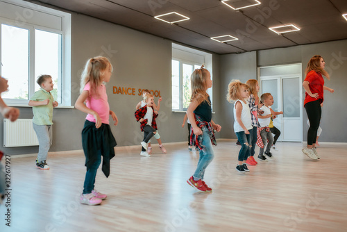 Repeat after me. Group of active children dancing in front of the large mirror while having choreography class in the dance studio. Female dance teacher and kids © Svitlana